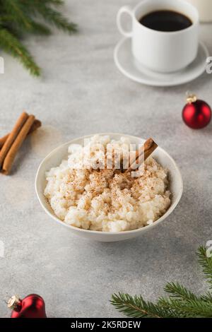 Skandinavischer Reisbrei mit Zimt in einer Schüssel, umgeben von Weihnachtskugeln. Frühstück am Heiligabend. Stockfoto