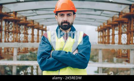 Ehrgeiziger Ingenieur, der Arme überquert und allein im Industriegebiet steht und die Kamera anschaut. Job abd Spezialisten Konzept. Stockfoto