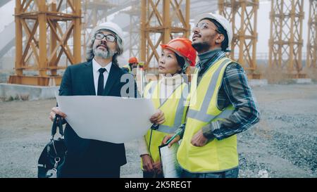 Architekt reifer Mann in Anzug diskutiert Projekt mit Bauherren tragen Uniform zeigen Bauplan stehen auf der Baustelle. Mitarbeiter- und Arbeitskonzept. Stockfoto