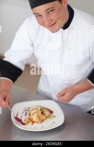 Mit dem letzten Schliff wird es perfekt. Yougn Chefkoch fügt einem zubereiteten Hühnergericht dekorative Zierarbeiten hinzu - Portrait. Stockfoto