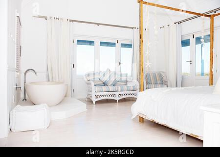 Moderne Version des klassischen Strandhauses. Blick auf ein Bad in der Ecke eines hellen weißen Schlafzimmers. Stockfoto