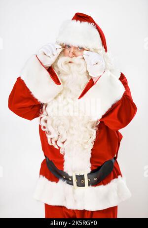 Ich überprüfe, ob Sie frech oder nett sind. Ernster Weihnachtsmann guckt auf weißem Hintergrund über seine Brille. Stockfoto