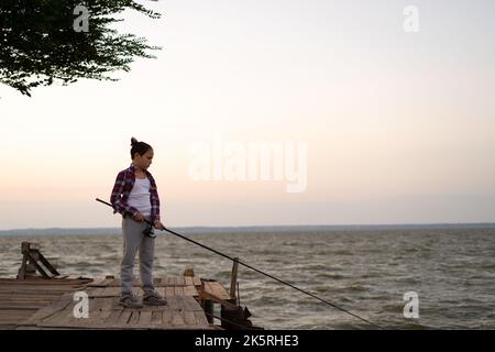 Junge angeln auf dem See bei Sonnenuntergang. Kinder Angeln Spinner Rute im Sommer. Stockfoto