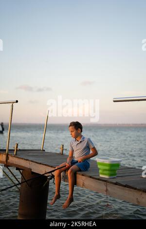 Junger netter Junge, der an einem Sommertag auf einem See fischt. Angeln Stockfoto