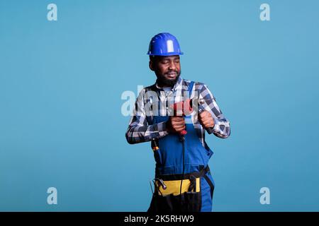 Studio-Porträt von afroamerikanischen Arbeiter in Overalls Arbeit einheitliche Schutzhelm hält Akku-Schraubendreher. Bauunternehmer, der Renovierung des Innenraums des Hauses macht. Stockfoto