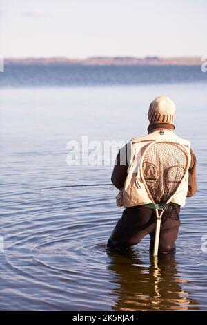 Warten auf den großen. Ein einsitzender Fischer steht knietief im Wasser. Stockfoto