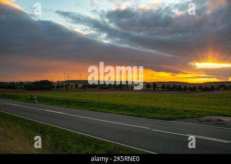 Sonnenuntergang über einer Straße, die durch landwirtschaftliche Flächen führt Stockfoto