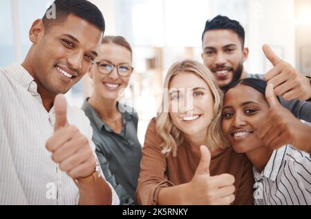 Porträt einer Gruppe selbstbewusster, diverser Geschäftsleute, die Daumen nach oben gestikulieren und gemeinsam in einem Büro Selfies machen. Fröhliche Kollegen, die lächeln Stockfoto