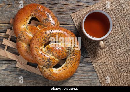 Weiche Brezeln mit Mohn und einer Tasse Tee auf einem alten Holztisch, Draufsicht Stockfoto