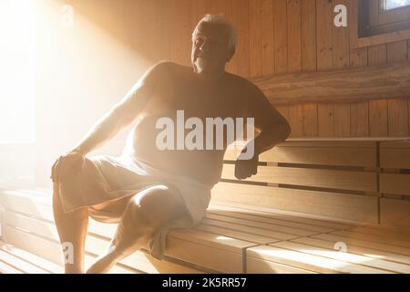 Mann in der Sauna. Dampf mit Sonnenlicht, Spa und Wellness-Konzept, entspannen Sie in der heißen finnischen Sauna. Stockfoto