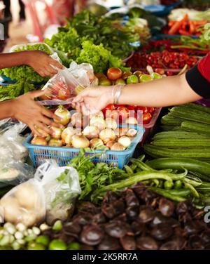 Lokale Händler zeigen ihre Waren. Nahaufnahme einer Frau, die für ihren Kauf an einem Gemüsestandstand in einem Markt - Thailand - bezahlt. Stockfoto