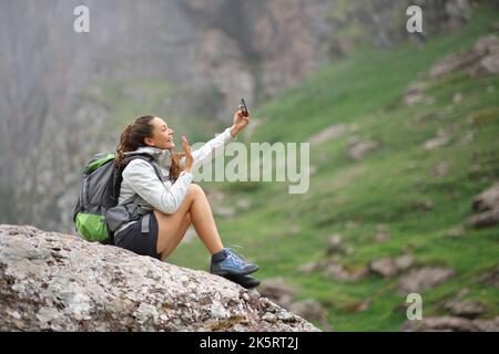 Glücklicher Wanderer, der Selfie mit dem Smartphone auf einem Felsen in den Bergen macht Stockfoto