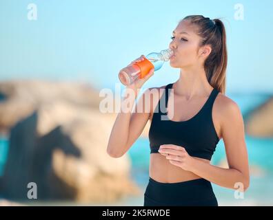 Schöne Frau, die am Strand Yoga praktiziert. Junge Sportlerin trinkt Wasser während sie draußen trainieren. Eine Pause einlegen. Suche nach innen Stockfoto