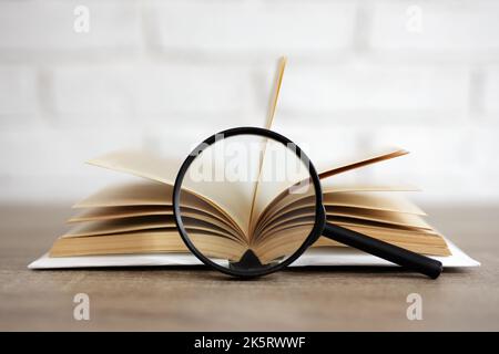 Bildungs- und Forschungskonzept - offenes Buch mit Lupe auf dem Tisch Stockfoto