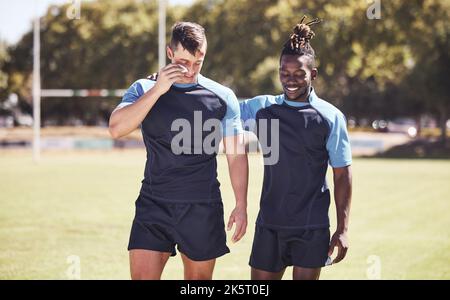 Zwei verschiedene junge Rugby-Spieler, die draußen auf dem Spielfeld stehen. Schwarzer Mann lächelt, während er mit seinem verletzten und verletzten kaukasischen Teamkollegen spricht. Sportlich Stockfoto