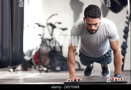 Ein junger hispanischer Mann, der während des Trainings in einem Fitnessstudio Bodyweight-Push-up-Übungen macht. Muskulös fokussierten Kerl tun drücken Sie ups und einen Plank halten zu bauen Stockfoto