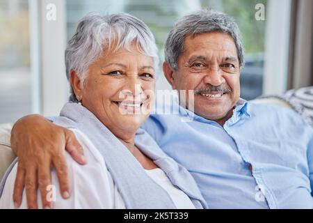 Porträt eines liebevollen, gemischtgeschlechtlichen Seniorenpaares, das sich zu Hause in seinem Wohnzimmer entspannt. Hispanischer Mann und Frau, die sich im Wohnzimmer auf dem Sofa verklebten Stockfoto