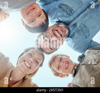 Nahaufnahme einer vierköpfigen Familie, die lächelnd nach unten blickt. Kaukasisches Paar, das sich mit ihren Söhnen beim Spielen in einem Garten oder Hinterhof eine Kuschelei teilt Stockfoto