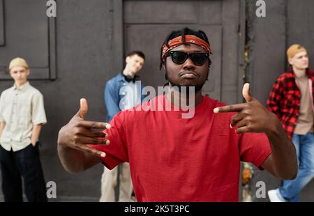 Das vielfältige Hip-Hop-Team gegen die schwarze Betonwand konzentriert sich auf afroamerikanische Männer, die Handgesten machen Stockfoto