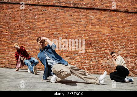 Porträt aller männlichen Breakdance-Teams, die im Freien im Sonnenlicht gegen eine Backsteinmauer posieren Stockfoto