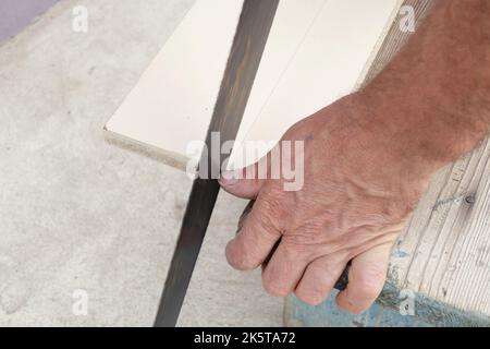 Mann, der im Garten mit Handsäge durch Holzbrett schneidet. Stockfoto