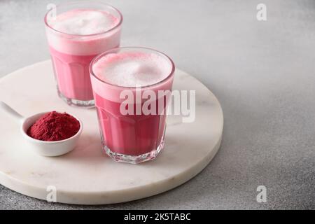 Rote Beete Latte oder rosa Mondmilch Latte in Gläsern aus Rote Bete Pulver und vegane Milch auf grauem Hintergrund. Trendiger, gesunder veganer Drink. Nahaufnahme. SPA kopieren Stockfoto