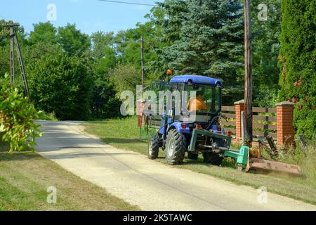 Kleiner kommunaler Traktor im Besitz der lokalen Behörden, der zum Schneiden von Grasrändern in der ländlichen Gasse des kleinen Weilers zala County ungarn verwendet wird Stockfoto