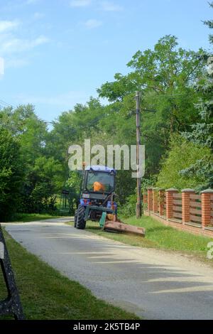 Kleiner kommunaler Traktor im Besitz der lokalen Behörden, der zum Schneiden von Grasrändern in der ländlichen Gasse des kleinen Weilers zala County ungarn verwendet wird Stockfoto