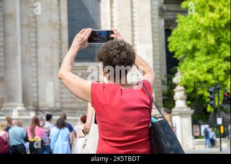 LONDON - 21. Mai 2022: Frau fotografiert mit dem Smartphone die St. Paul's Cathedral. Ihr Foto ist auf dem Bildschirm des Geräts sichtbar Stockfoto