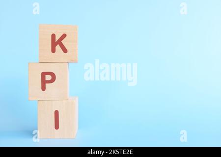 KPI oder Key Performance Indicator Business Target und Establishment Concept. Menschliche Hand stapelt Holzblöcke auf blauem Hintergrund. Stockfoto