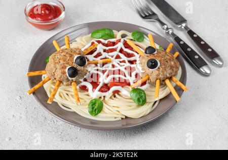 Koteletts sehen aus wie Spinnen mit Olivenaugen und Trinkhalmen, serviert mit Spaghetti-Nudeln und Tomatensauce auf hellgrauem Hintergrund. Halloween-Frühstück Stockfoto