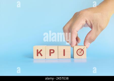 KPI oder Key Performance Indicator Business Target und Establishment Concept. Menschliche Hand stapelt Holzblöcke auf blauem Hintergrund. Stockfoto