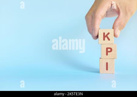 KPI oder Key Performance Indicator Business Target und Establishment Concept. Menschliche Hand stapelt Holzblöcke auf blauem Hintergrund. Stockfoto