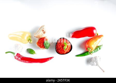 biber Salcasi-Pfefferpaste im türkischen Stil. Schwarze Schüssel mit roter Sauce und frischer Paprika auf weißem Hintergrund isoliert Stockfoto