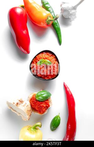 Eine Schüssel mit Chilisauce auf weißem Hintergrund. Würziger Ajika mit Chilischoten auf weißem Hintergrund. Stockfoto