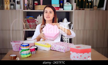 Geschenkverpackung. Attraktive Frau, Designer von Geschenken und Dekorationen zeigt Training online, zeichnet Videoblog, Webinar, sitzt vor dem Smartphone, Kamera. Online-Verkauf. Hochwertige Fotos Stockfoto