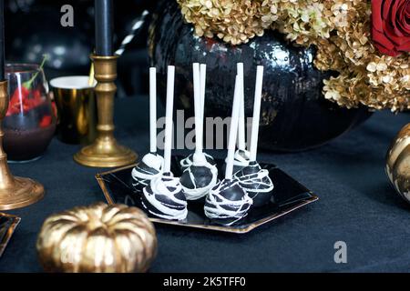 Desserttisch für Halloween. Cake Pops mit Themenmotiven. Goldener Kürbis und goldene Blumen Dekoration. Stockfoto