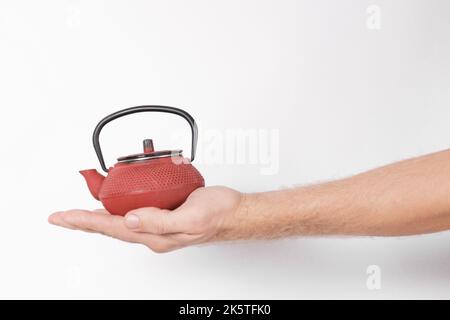 Die Hand des Mannes hält eine rote chinesische Teekane auf weißem Hintergrund Stockfoto