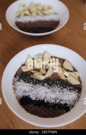 Veganer Rohporridge aus Leinsamen mit Früchten und Chia, schwarzen Sesam- und Flockensamen, Kokosflocken. Gesunde, nahrhafte und frische Lebensmittel. Zwei Platten Stockfoto