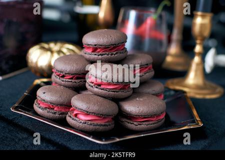 Braune Schoko-Makronen mit rosa Füllung. Waldbeeren in Cremefarben. Stockfoto