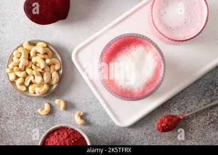 Gesunder veganer Bio-Rote-Beete-Latte mit Cashewnüssen-Milch auf grauem Hintergrund. Tolles wärmendes Getränk. Blick von oben. Speicherplatz kopieren. Trendiges, gesundes dri Stockfoto