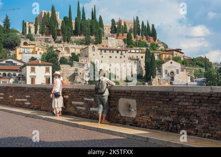 Ponte di Pietra Brücke, Blick auf die Menschen, die auf der Ponte Pietra stehen und auf den Hügel San Pietro am nördlichen Etschufer, Verona, Italien, blicken Stockfoto