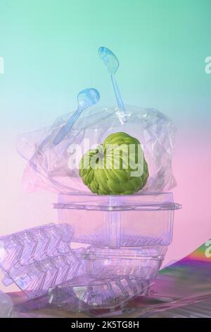 Stillleben mit Cherimoya Obst und Plastikmüll. Das Thema Mikroplastik in Lebensmitteln. Mit dem Effekt der Photoelastizität. Pastellfarben in Regenbogenfarben Stockfoto