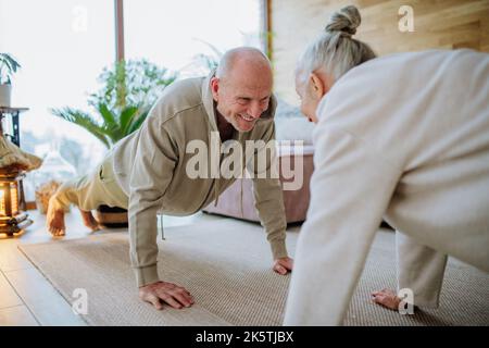 Ältere Paare trainieren gemeinsam in ihrem Wohnzimmer während des kalten Herbsttages. Stockfoto
