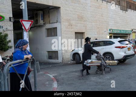 Jerusalem, Israel - 28.. September 2022: Ein Mann, der einen Kinderwagen benutzt, um Sukkah-Materialien auf einer Straße in Jerusalem, Israel, zu transportieren. Stockfoto