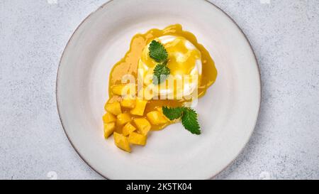 Panorama-Panna Cotta von oben mit natürlicher Vanilleschote, Mango-Sirup und Minze, High-Key Stockfoto