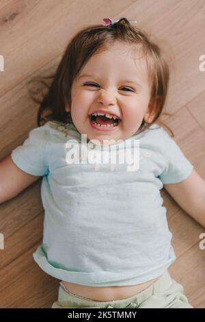 Nahaufnahme eines niedlichen Mädchens, das auf dem Rücken auf dem Holzboden liegt. Glückliches, lächelndes Kind. Platz für Text. Hochwertige Fotos. Glücklich lächeln Stockfoto