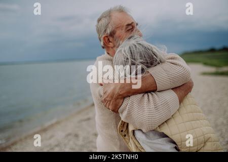 Ein verliebten Senioren-Paar umarmt sich gegenseitig und hat einen romantischen Moment in der Nähe des herbstlichen Meeres. Stockfoto
