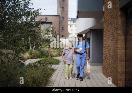 Glücklicher Betreuer, der mit seiner älteren Kundin aus dem Lebensmittelgeschäft zurückkehrte. Stockfoto