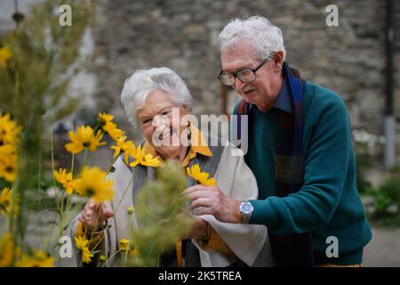 Glückliches Seniorenpaar beim herbstlichen Stadtspaziergang, posiert mit Blumen. Stockfoto